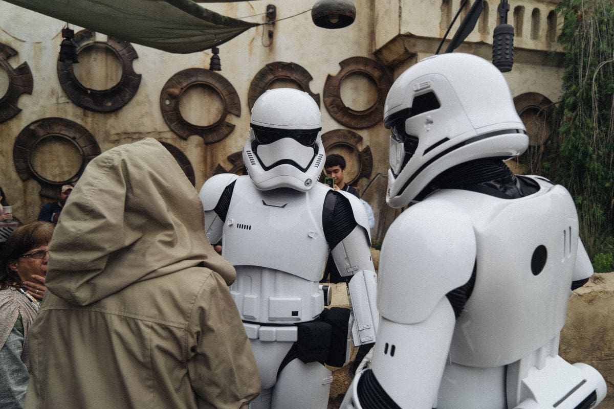 Two people in Stormtrooper costumes and a person in a hood facing each other