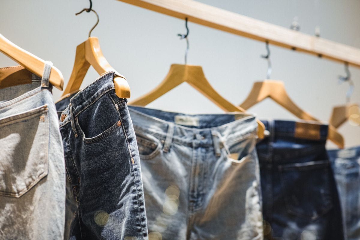 Multiple pants in wooden hangers hanging from a wooden rack