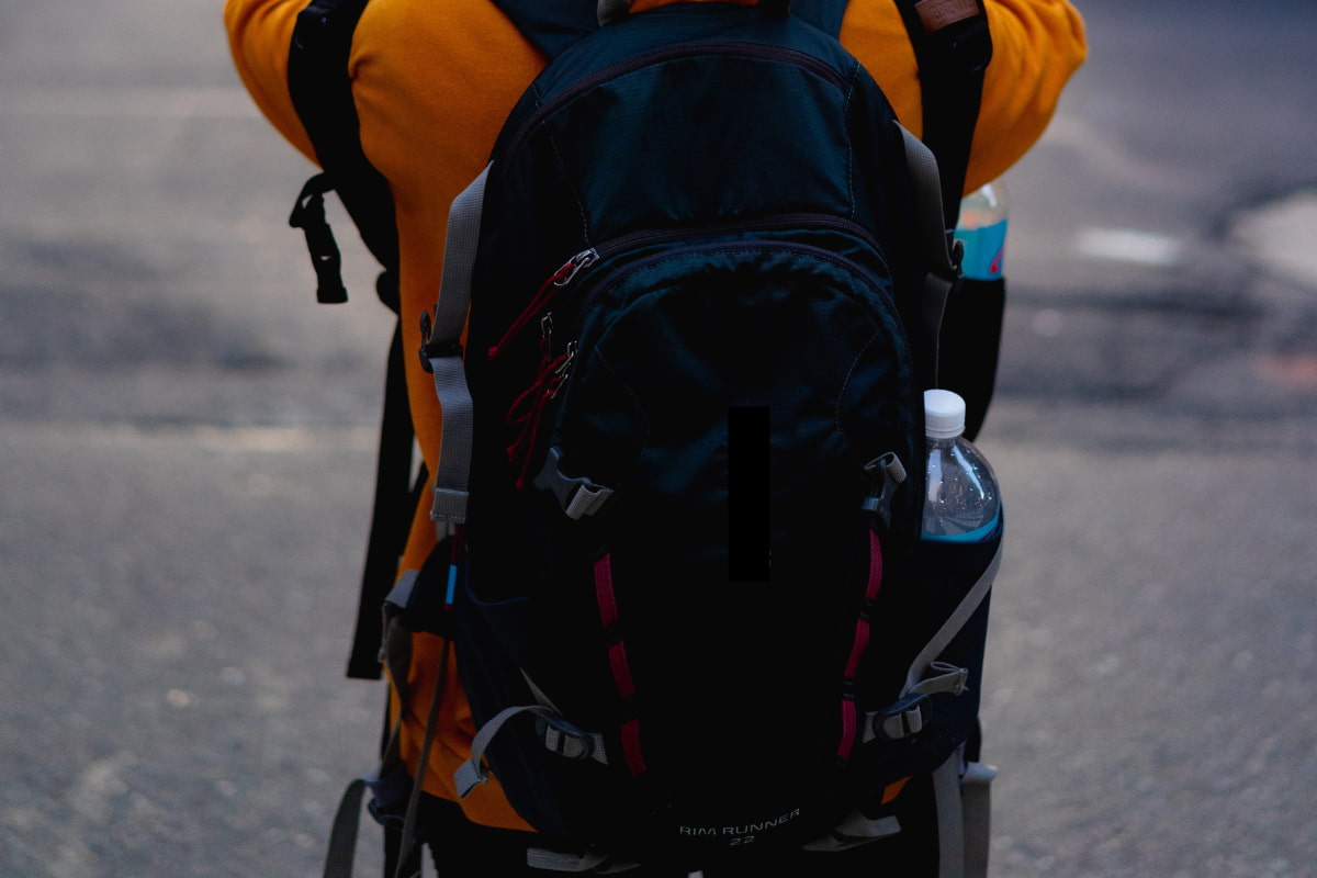 Person in an orange jacket wearing a backpack with a water bottle on the side