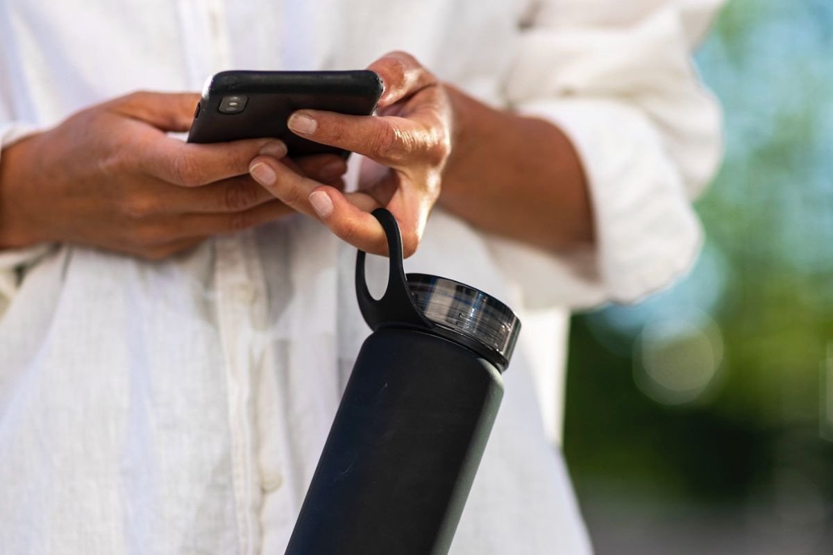 Person carrying a water bottle while using a phone