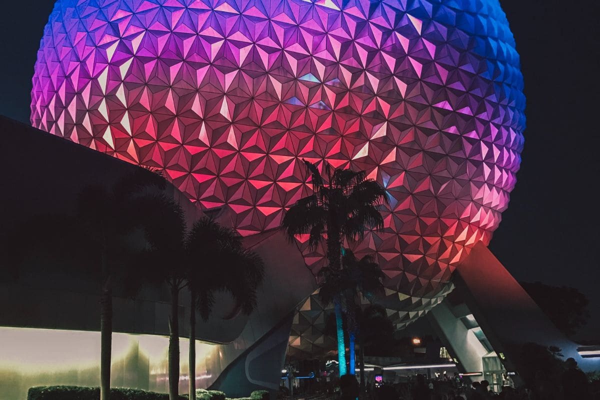 Silhouette of palm trees near the base of the illuminated Epcot Sphere at night