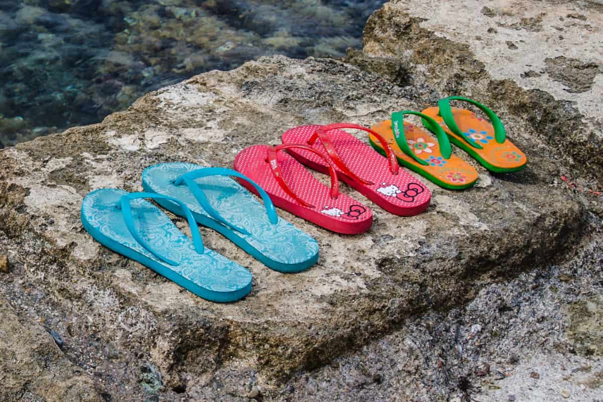Three pairs of flip flops on concrete near a body of water