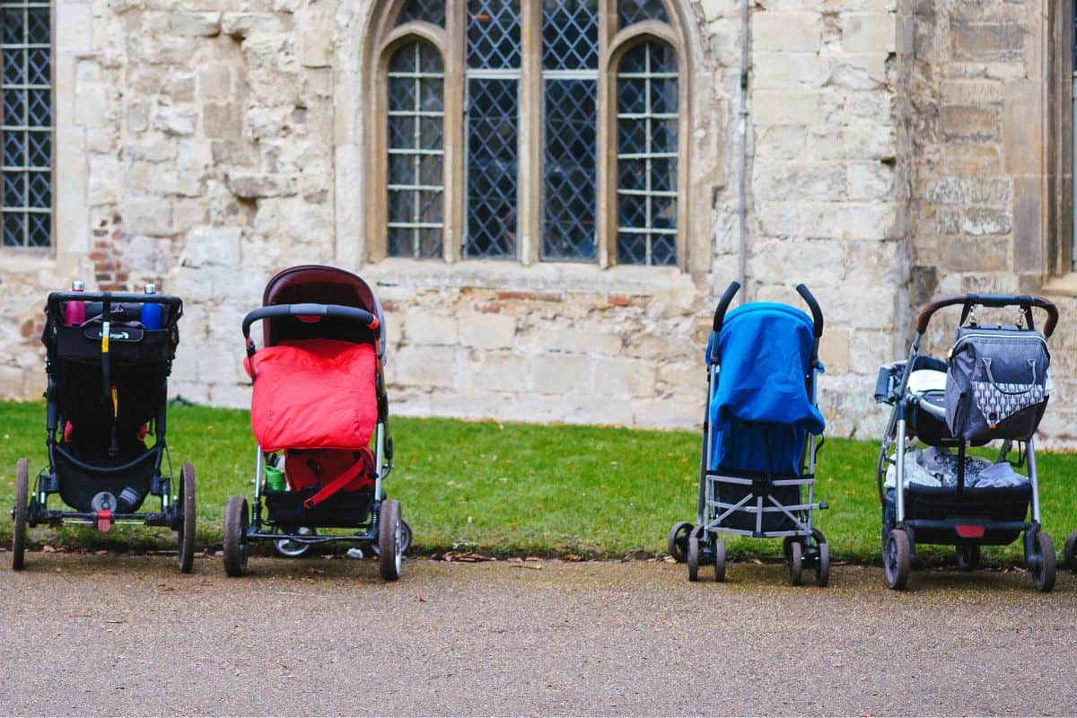 Four empty strollers parked on the side of a grassy lawn