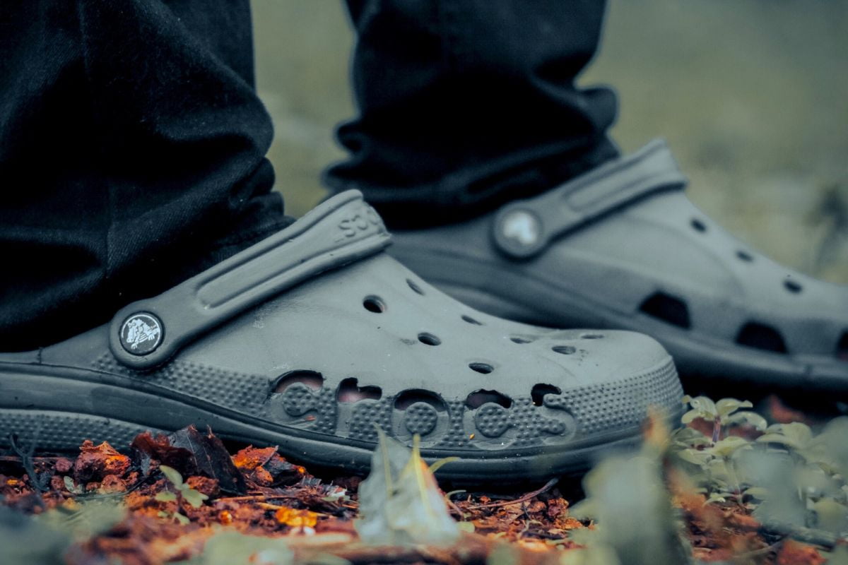 close up of person's feet wearing grey Crocs stepping on fallen leaves