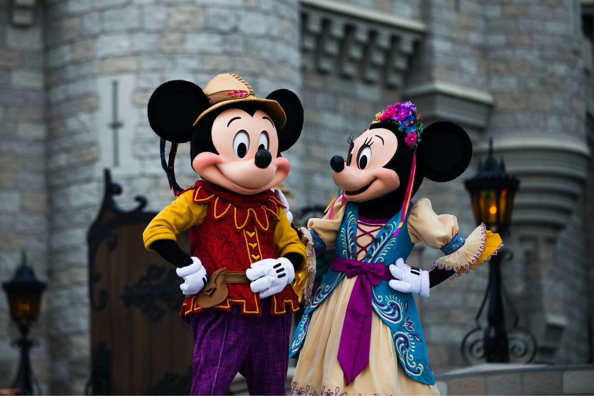 Two people in medieval themed Mickey and Minnie costumes in front of a castle