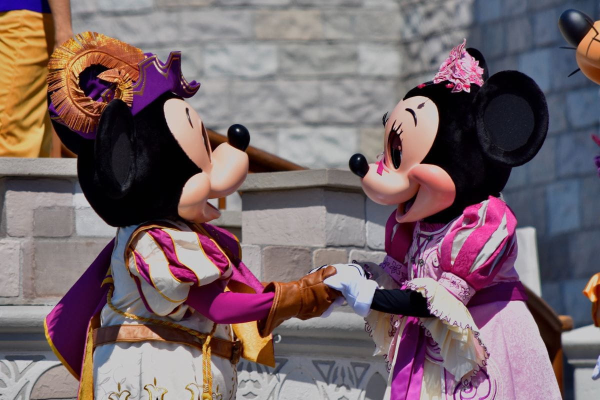 Two people in Mickey Mouse and Minnie Mouse costumes holding hands