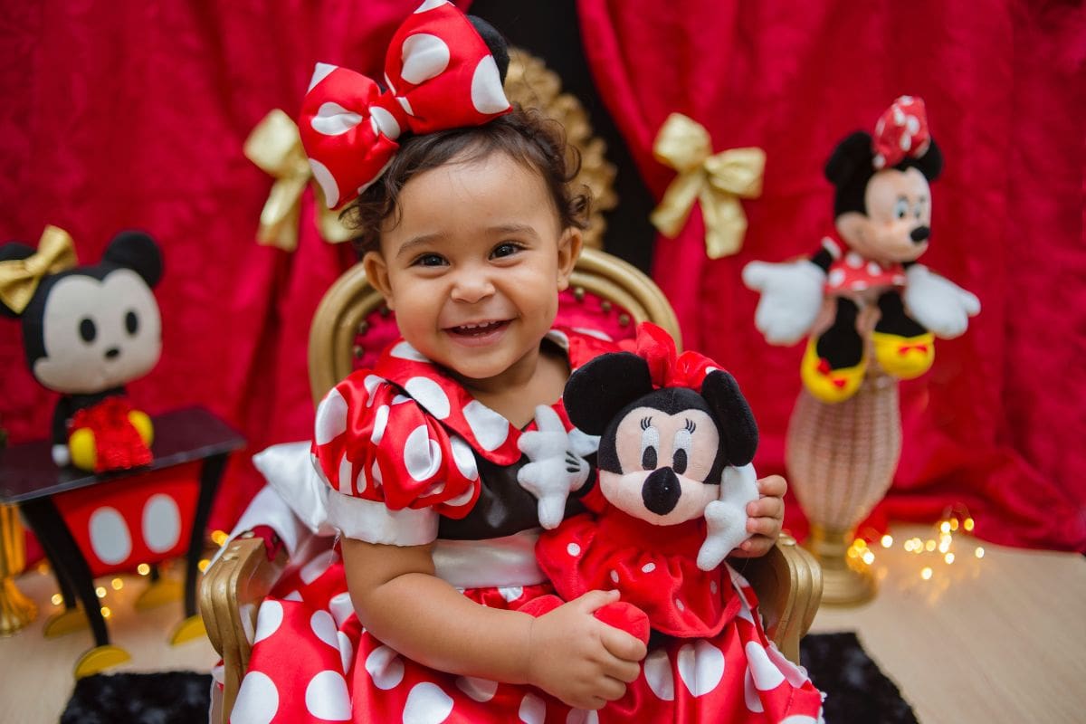 Small child in a Minnie Mouse outfit surrounded by Minnie Mouse stuffed toys