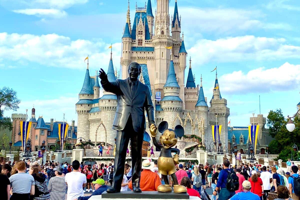 Statue of Walt Disney and Mickey Mouse amongst a crowd of people in front of the Castle at Disney World