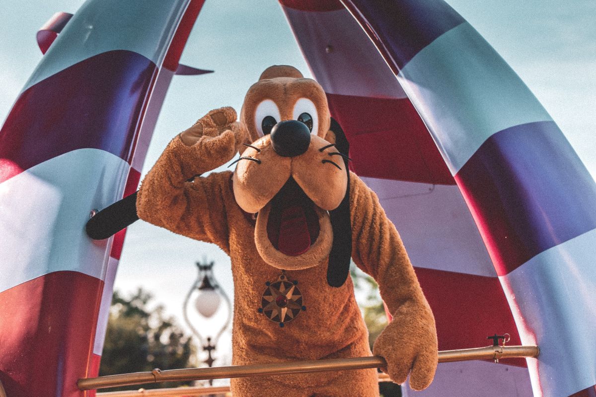 Person in a Pluto costume looking at the camera and waving to say hello