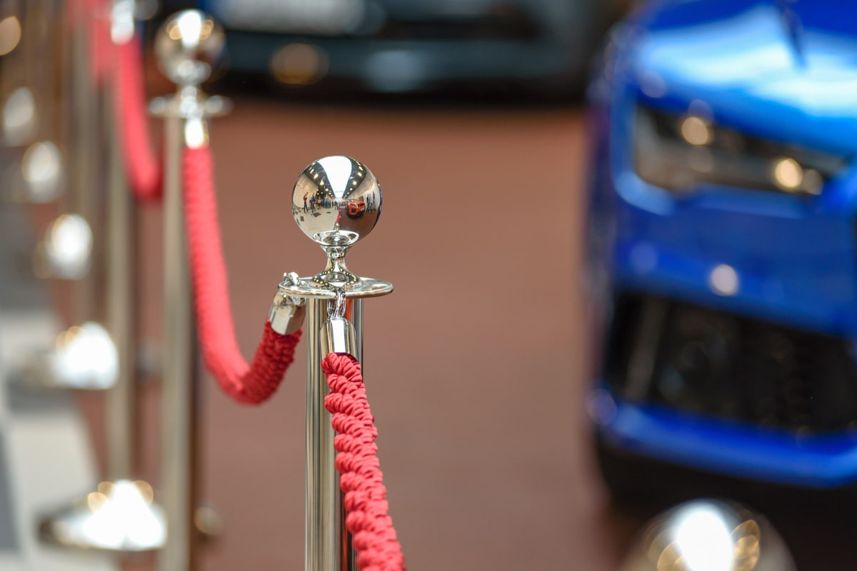 Red ropes attached to stanchions acting as barrier with a blue car in the background