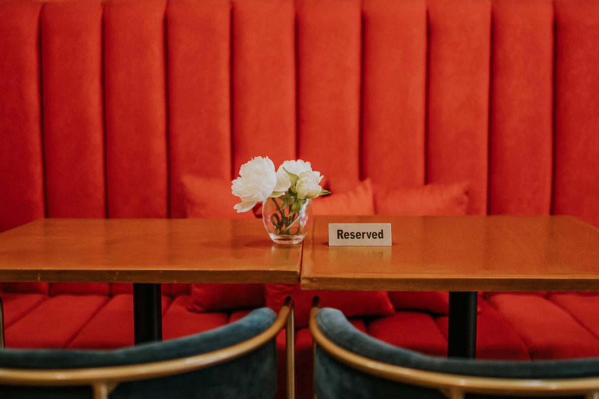 Reserved sign on a dining table with a flower in a vase and red cushion seats