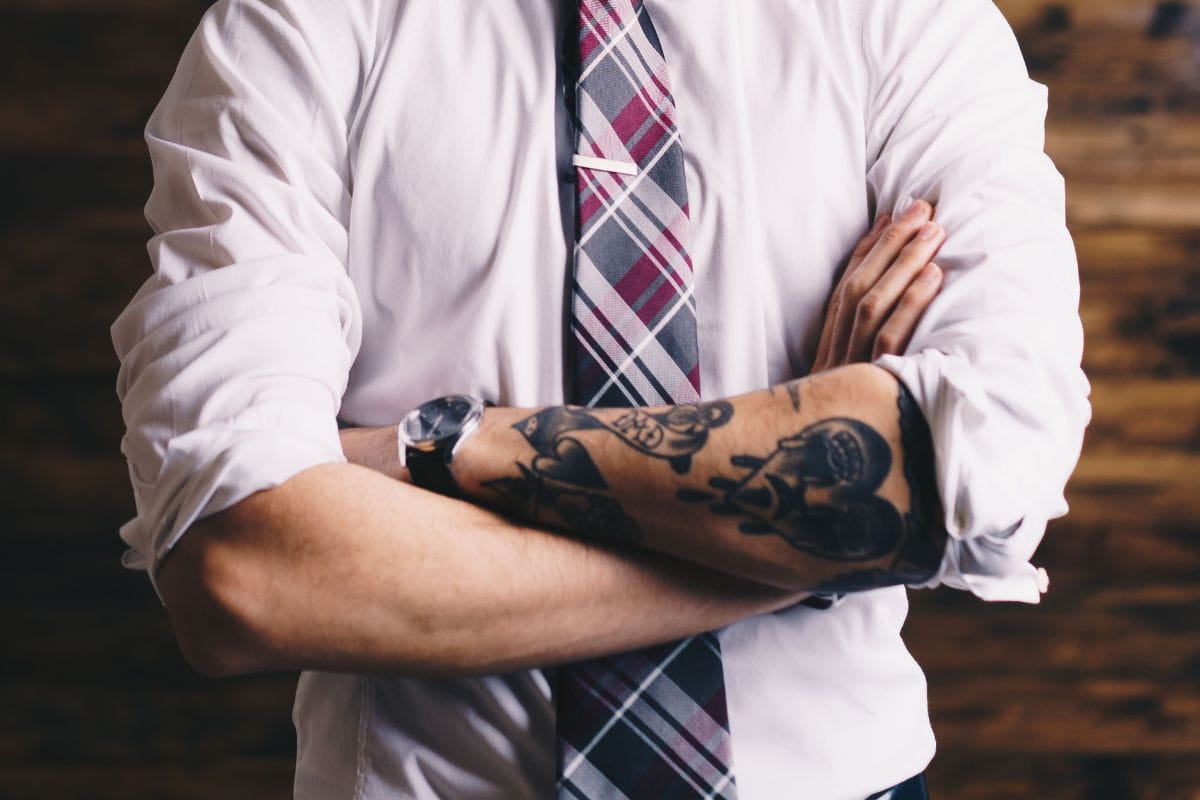 Person with tattooed arms wearing a white shirt with rolled-up sleeves and a tie