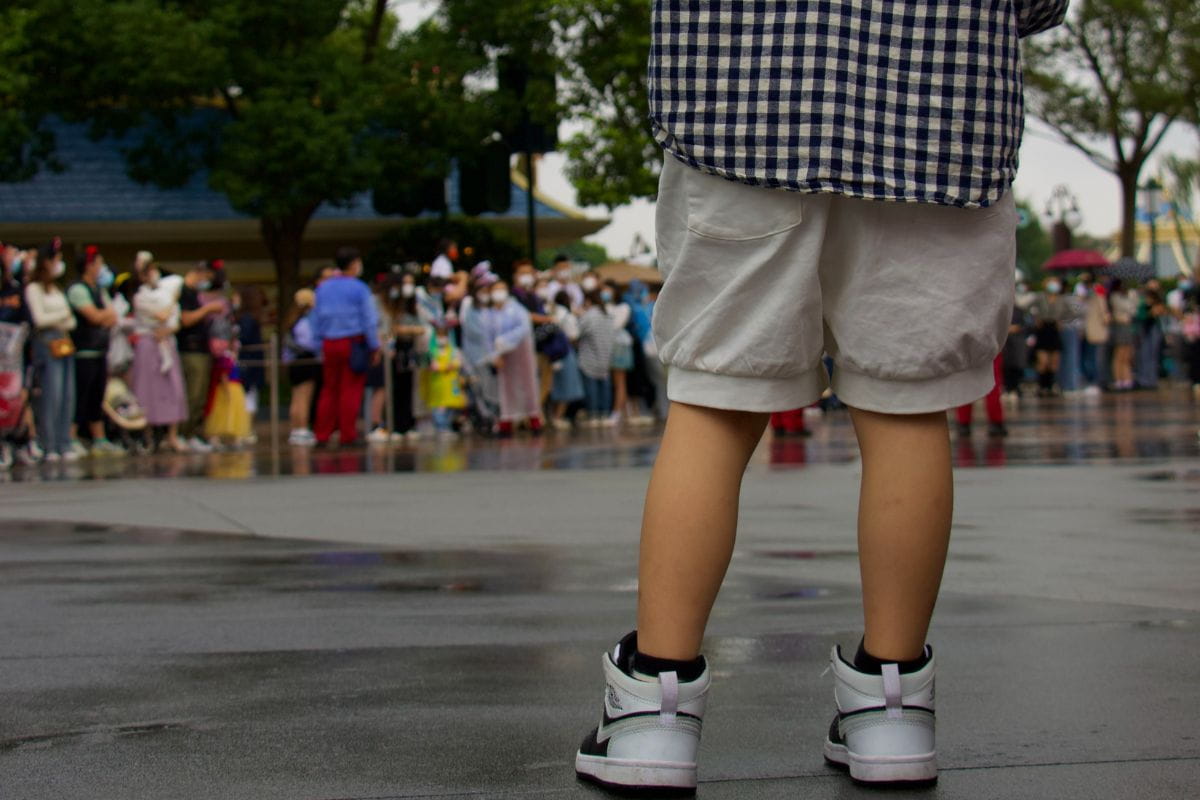 Child standing alone looking at a crowd of people from afar