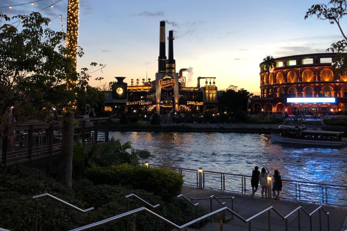 Three people looking from across the water at Universal Studios Orlando during sundown