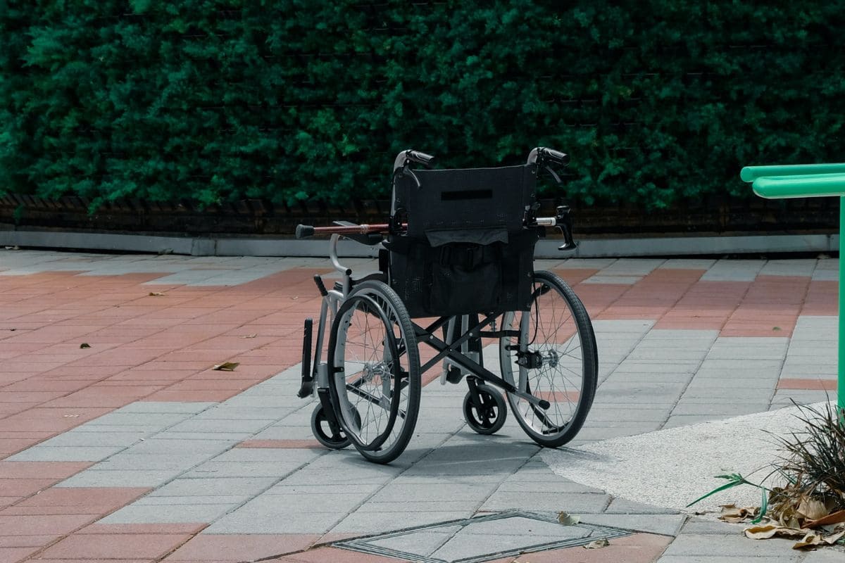 Empty wheelchair facing away from the camera with a walking cane on top of the armrest