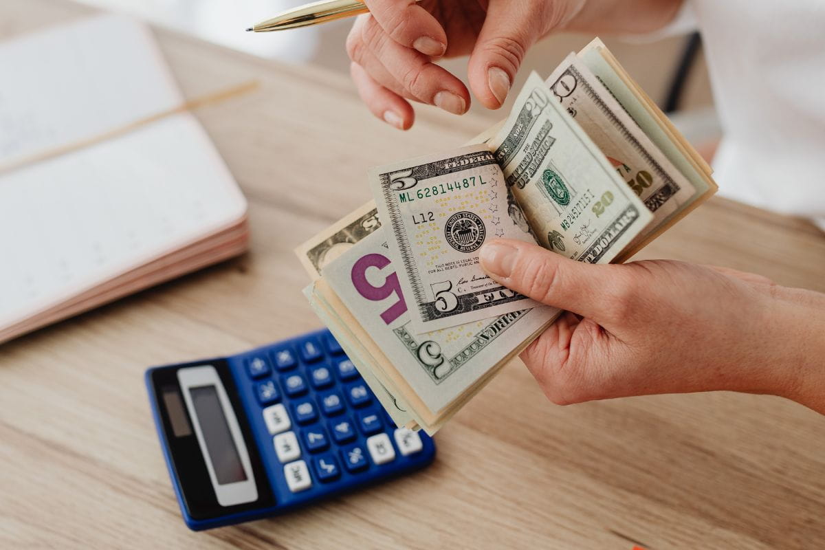 Hands of a person holding a pen and counting cash with a calculator on a wooden table
