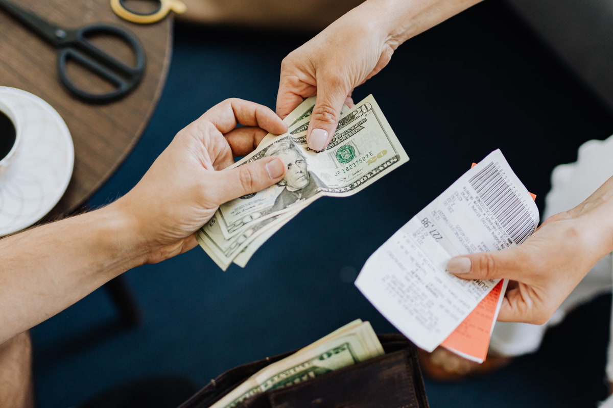 Close up of a person's hand giving cash to another person who is holding a receipt