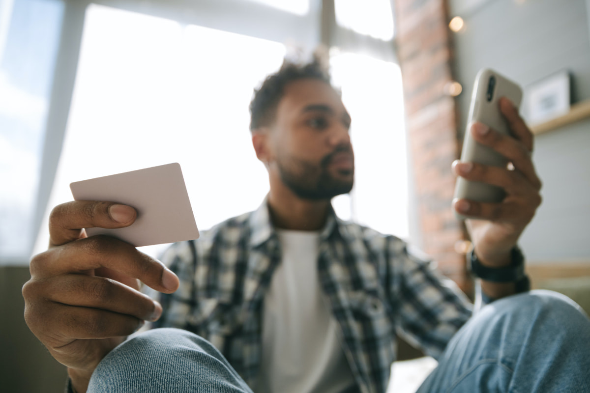 Man sitting down while checking his phone and holding a card