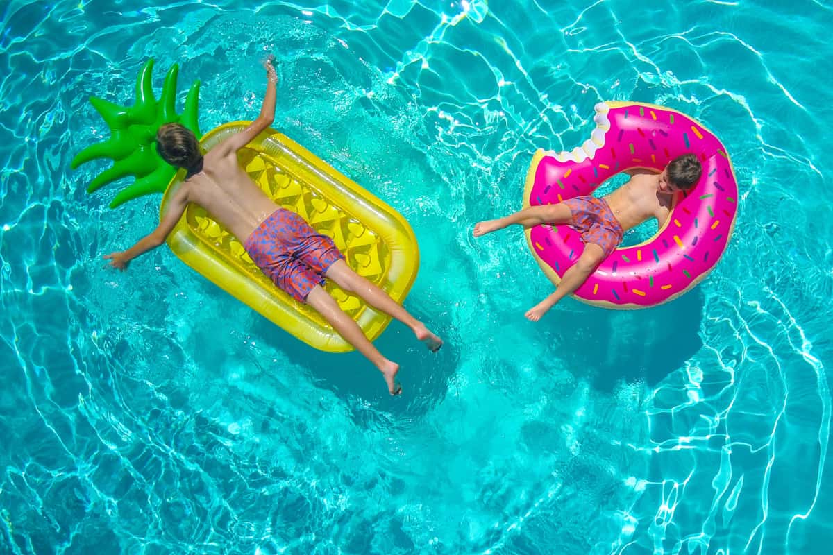Two children in a pool riding colorful pool floats