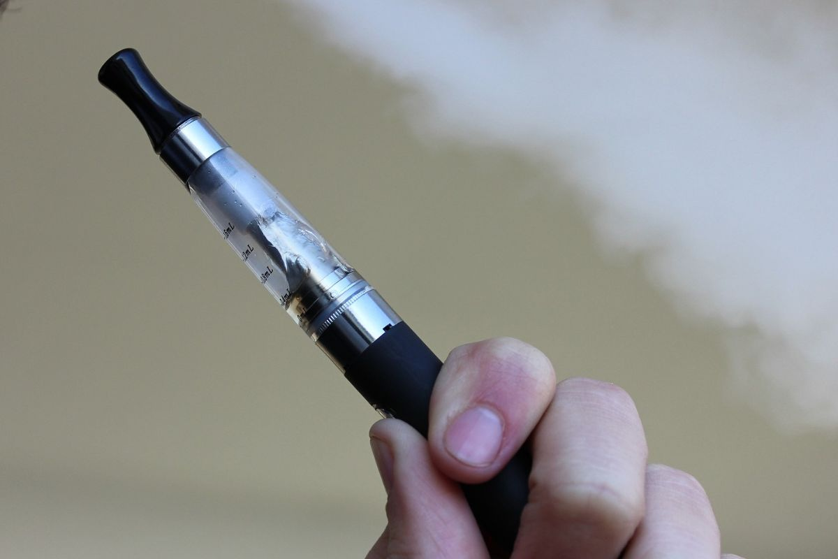 Close up of a person's hand holding an electronic cigarette with a little smoke in the background