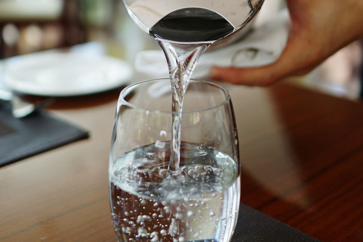 Person pouring water from a pitcher into a glass on a table