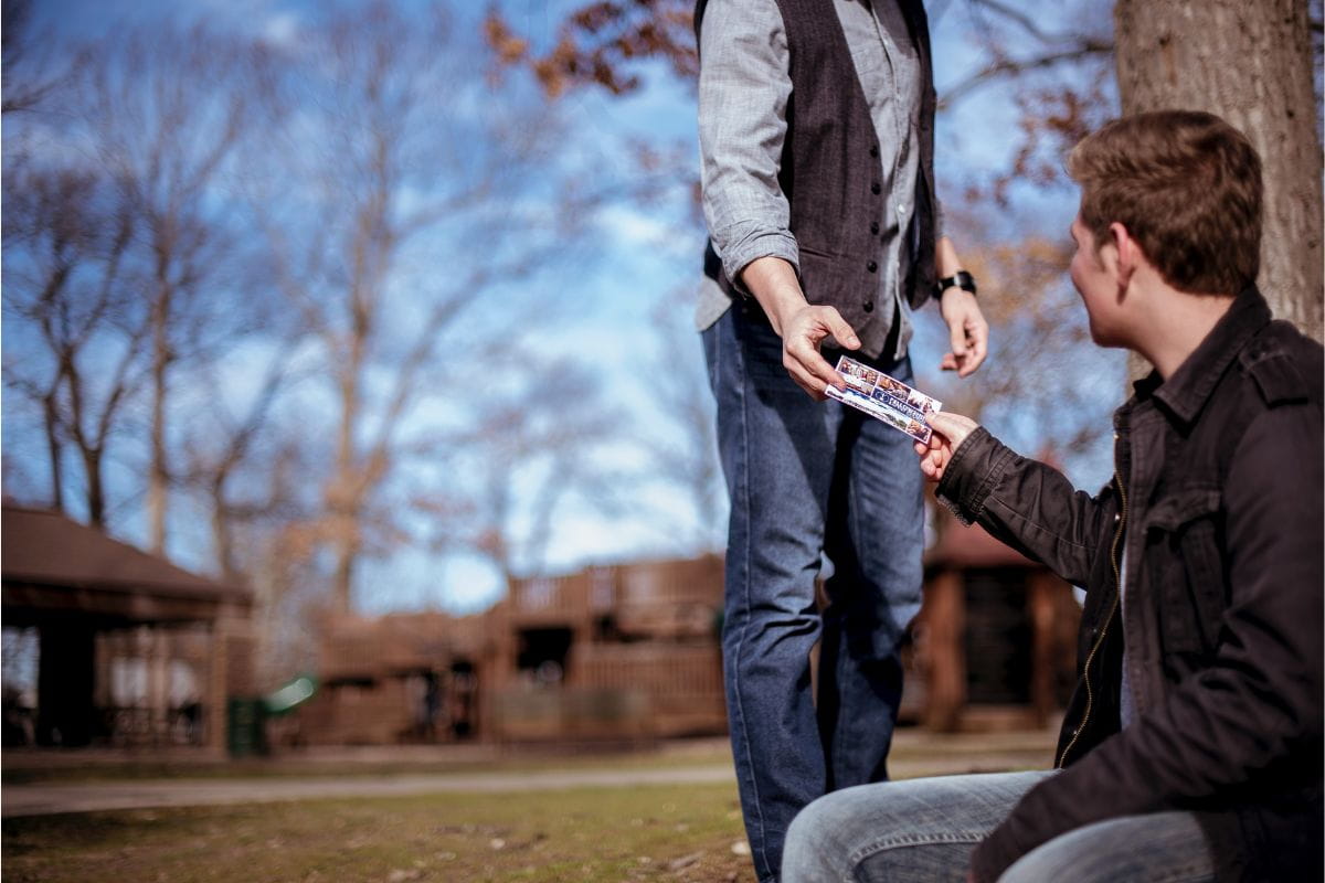 Person handing over a ticket to another person sitting on a park bench
