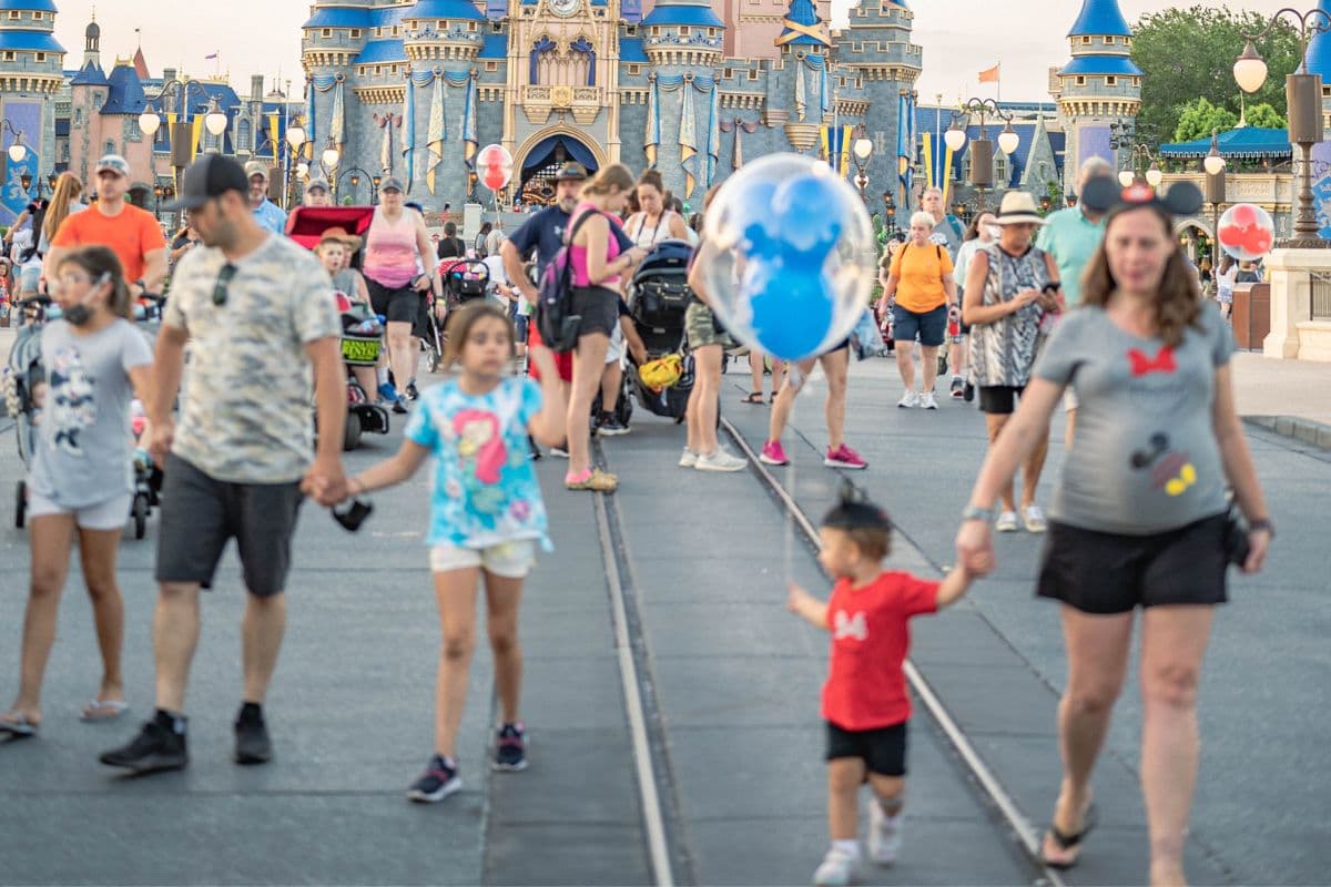 Children holding their parents' hands walking in front of the Disney Castle