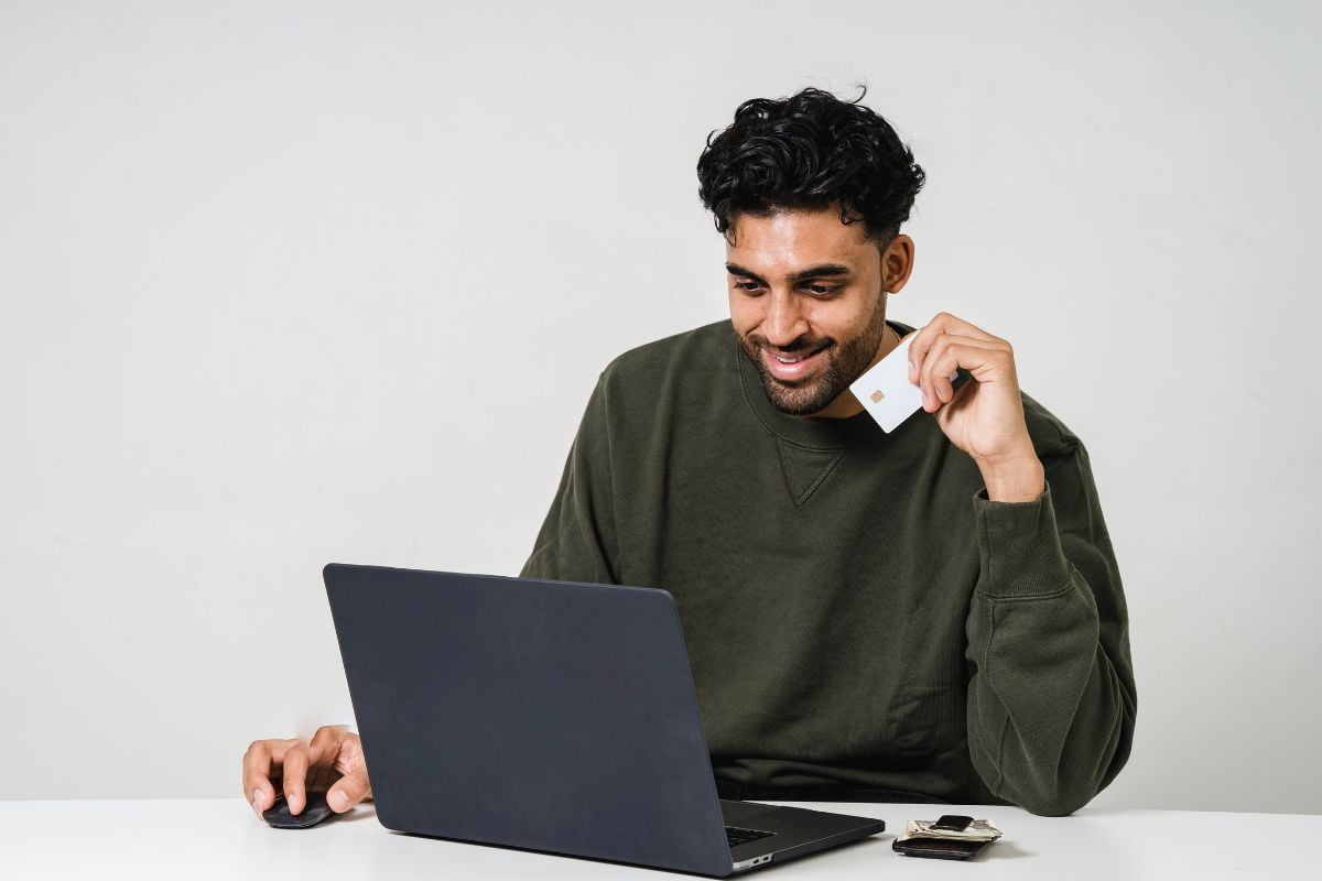 Man in front of laptop holding a credit card purchasing something online