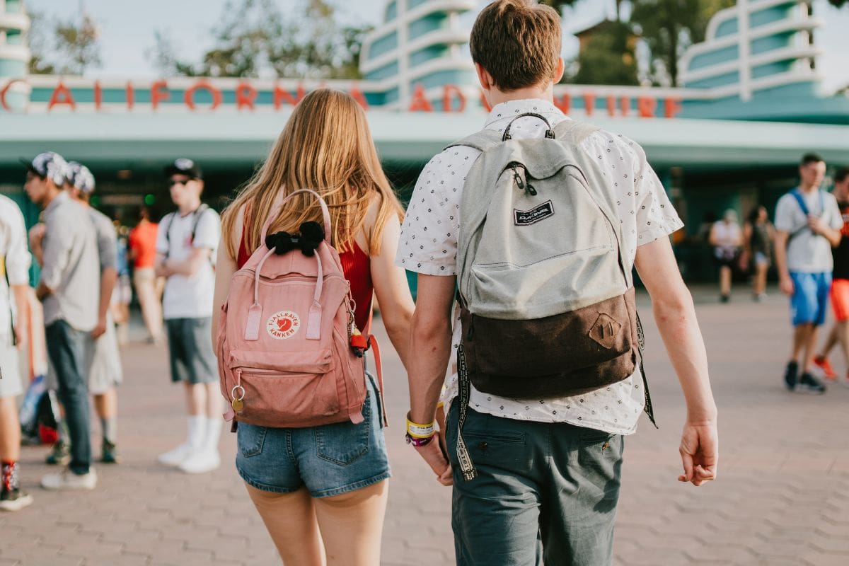 Two people wearing pink and grey backpacks walking together while holding hands