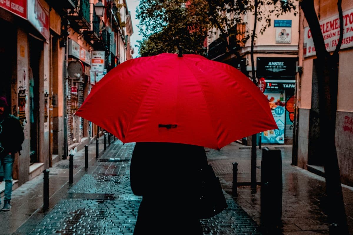 Person walking down a street using a red umbrella