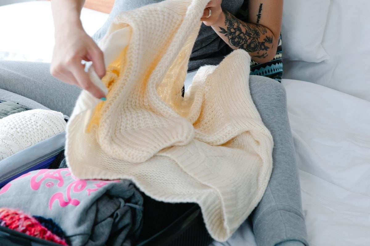 Person folding a white knitted sweater and packing it into a suitcase