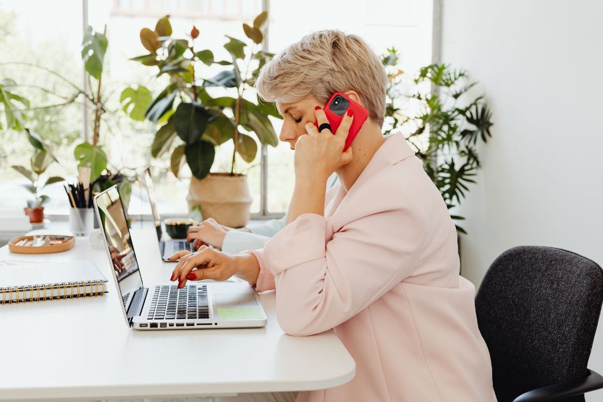 Woman sitting at a desk talking on a phone while working on a laptop