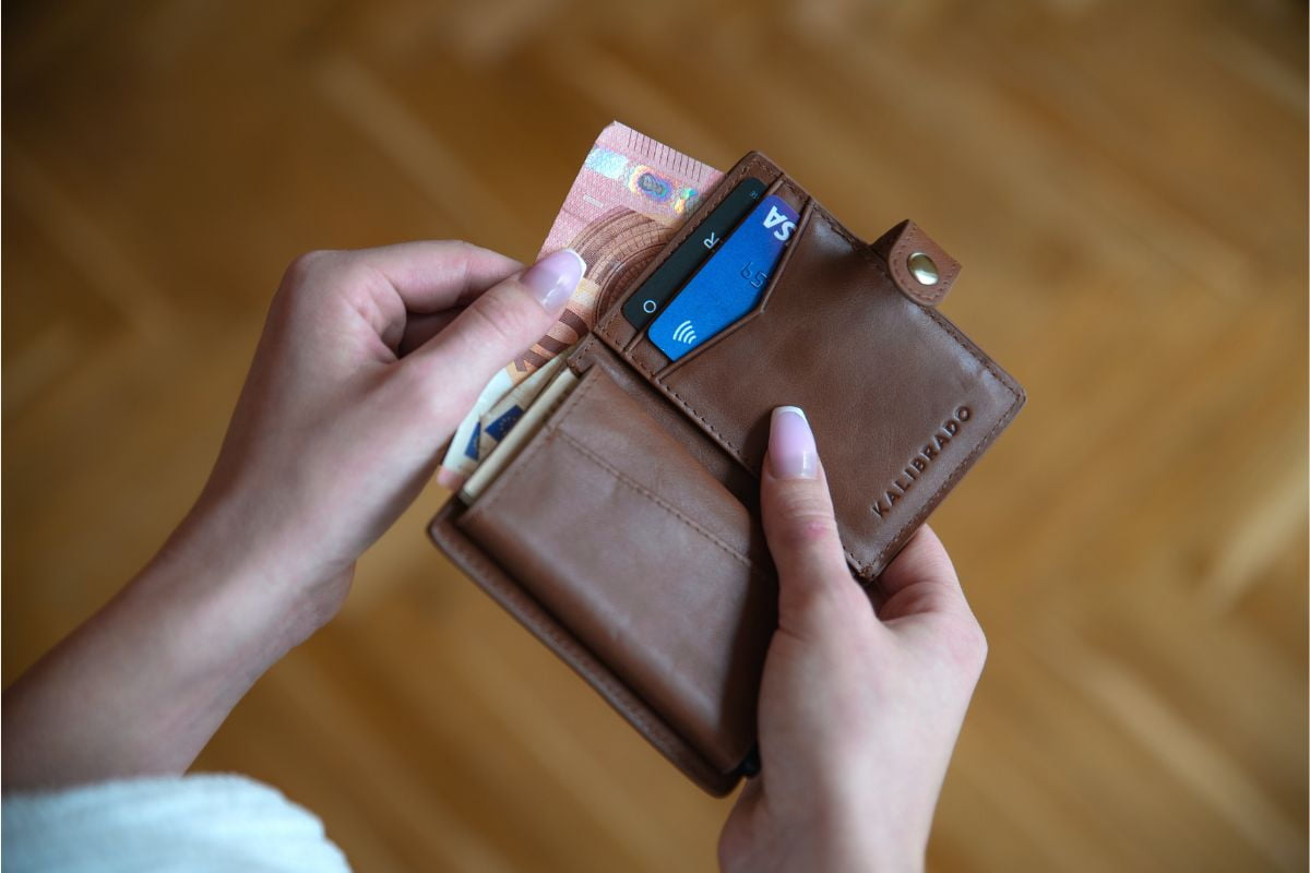 Person holding a wallet containing cash and cards