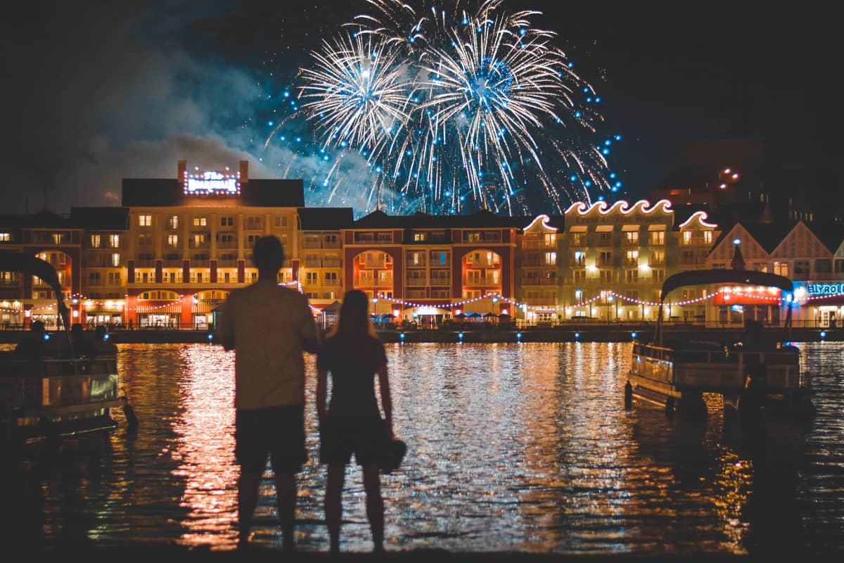 Two people watching fireworks near boats on a body of water