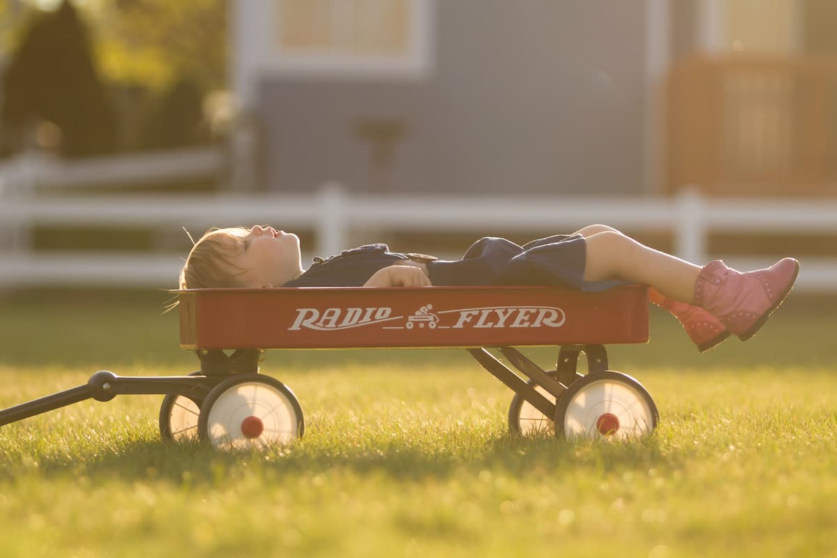 A child in pink boots is lying in the red wagon. 