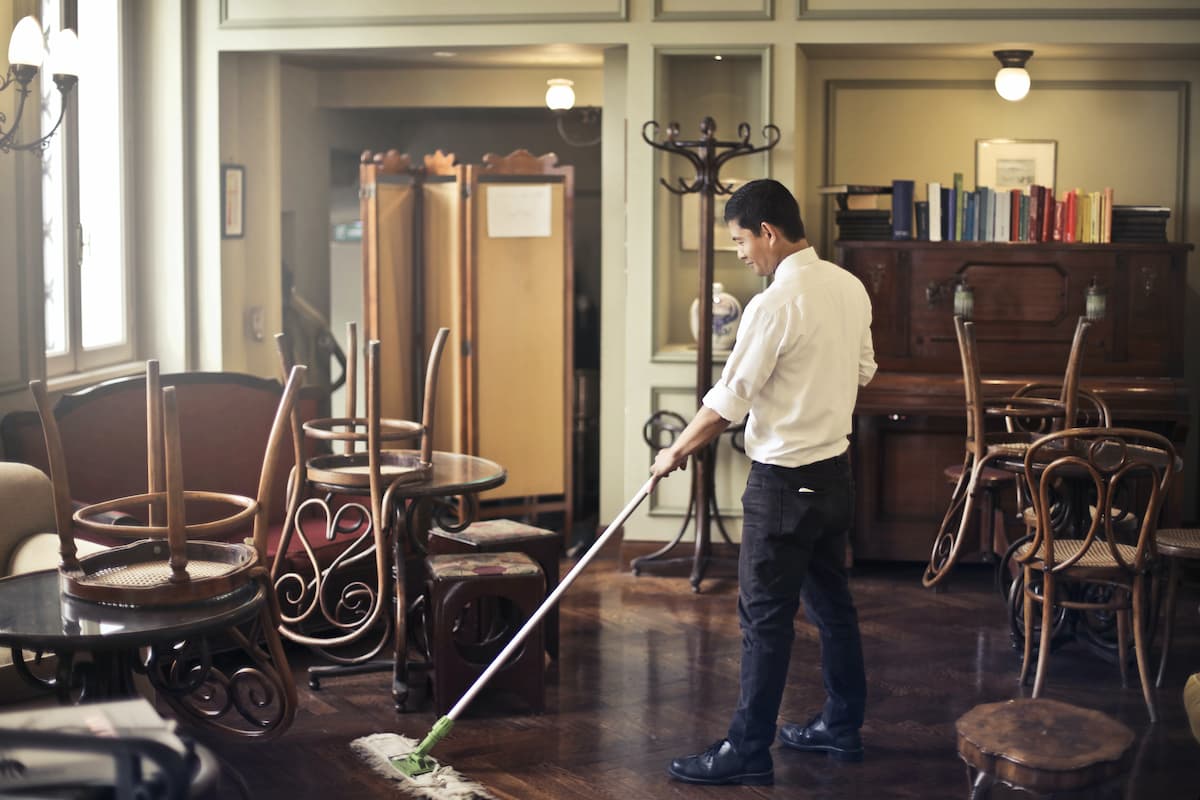 A male employee is mopping the floor in a restaurant. 