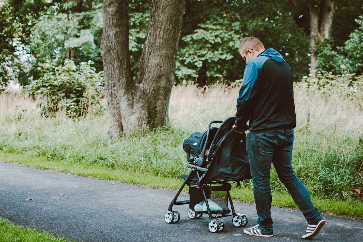 A man is pushing a baby in a stroller at the park.
