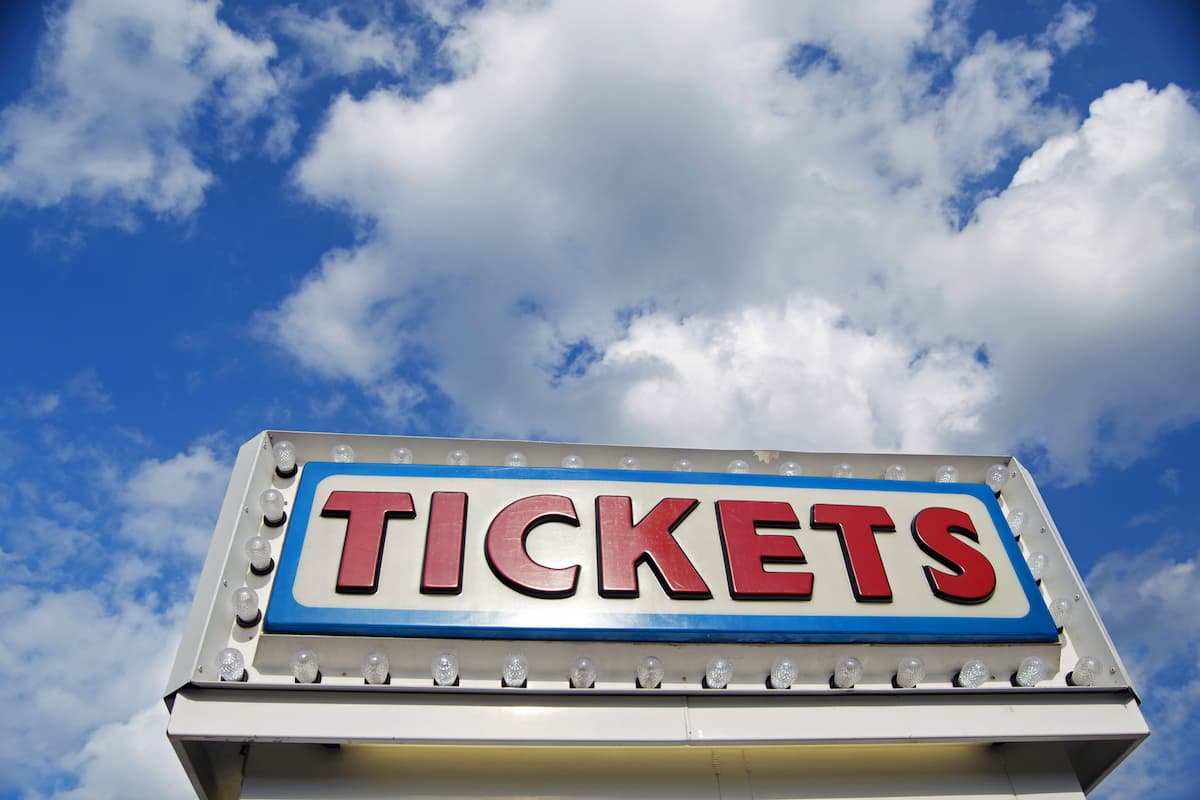 The word Tickets is at the top of a ticket booth with clouds and a blue sky. 