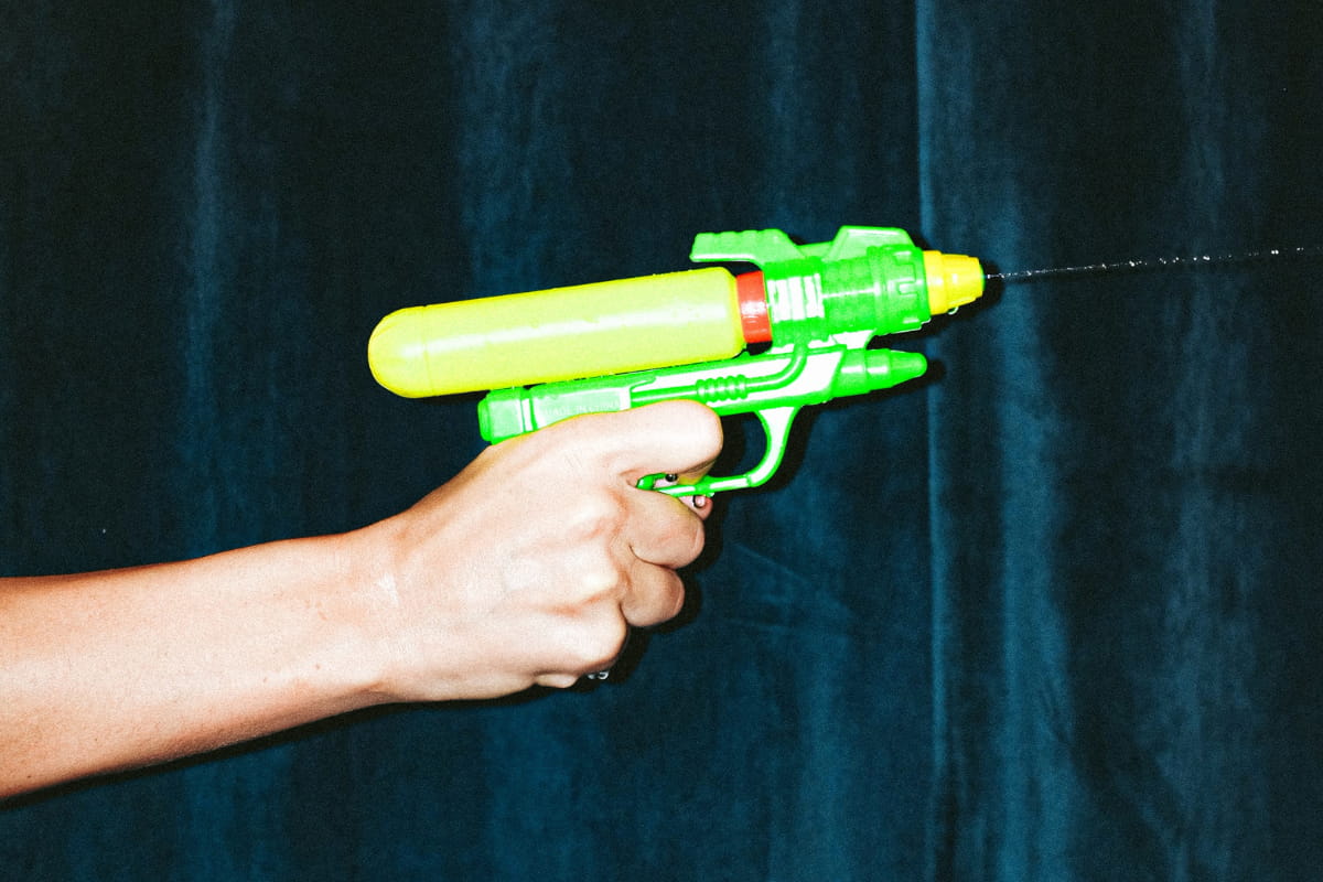 Person's hand holding a green and yellow plastic water gun or squirt gun