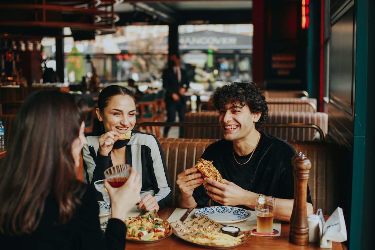 Two women and a man are laughing and eating at a restaurant. 