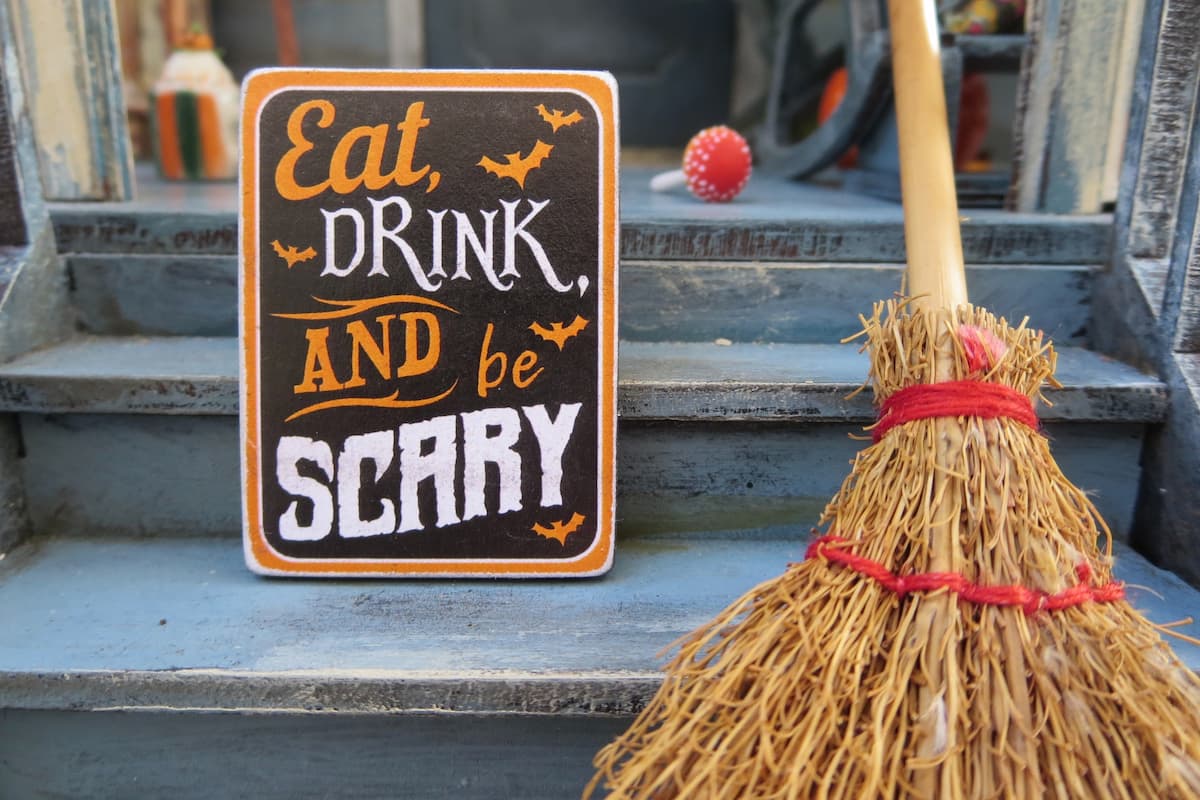 Close-up photo of a Halloween sign beside a broom with "Eat, Drink, and be SCARY" written on it. 