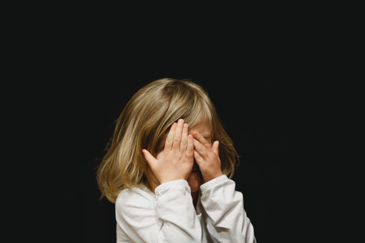 A scared girl is covering her face with both hands.