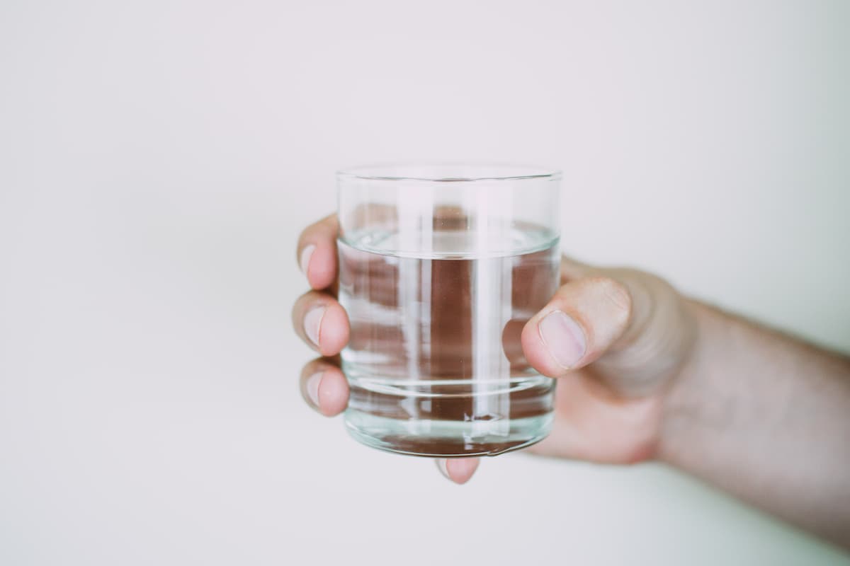 Close-up photo of a person's hand holding a glass of water on a white background. 