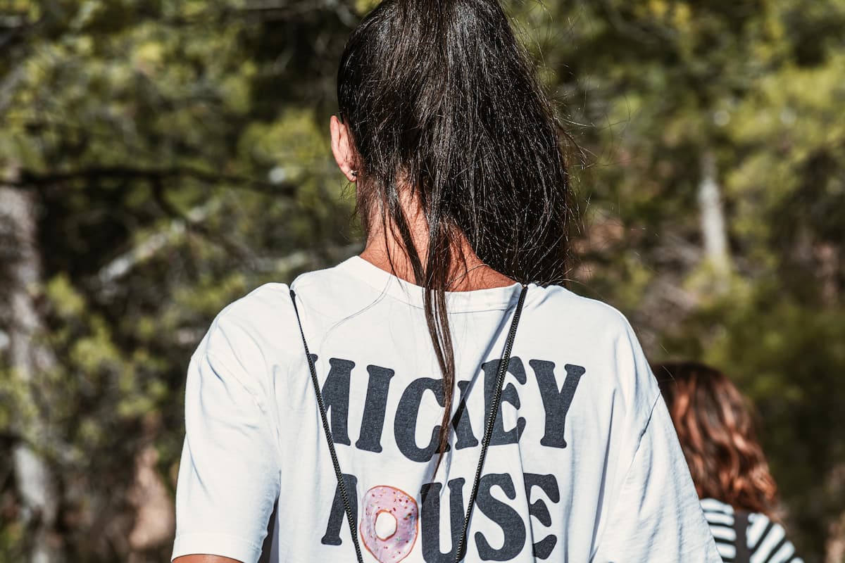 Back view of a woman wearing a white t-shirt with Mickey Mouse written on it.