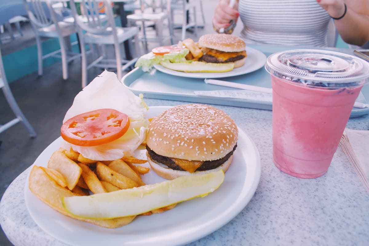 Cropped photo of a woman eating a burger and fries with a smoothie on the table. 