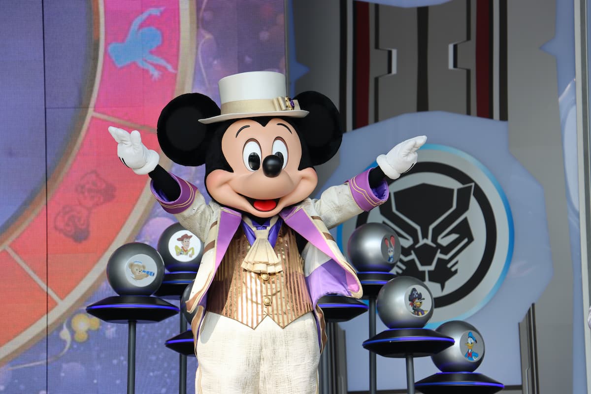 Mickey Mouse is standing on a stage with his hands raised.