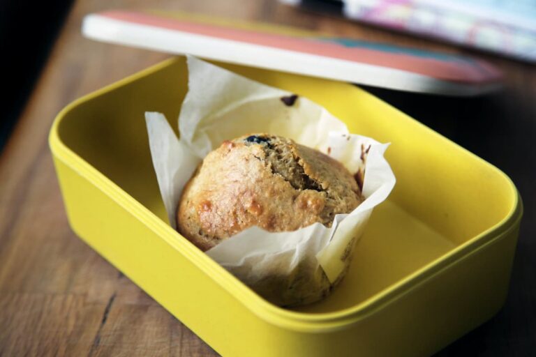 A muffin in a yellow lunch box on the wooden table.