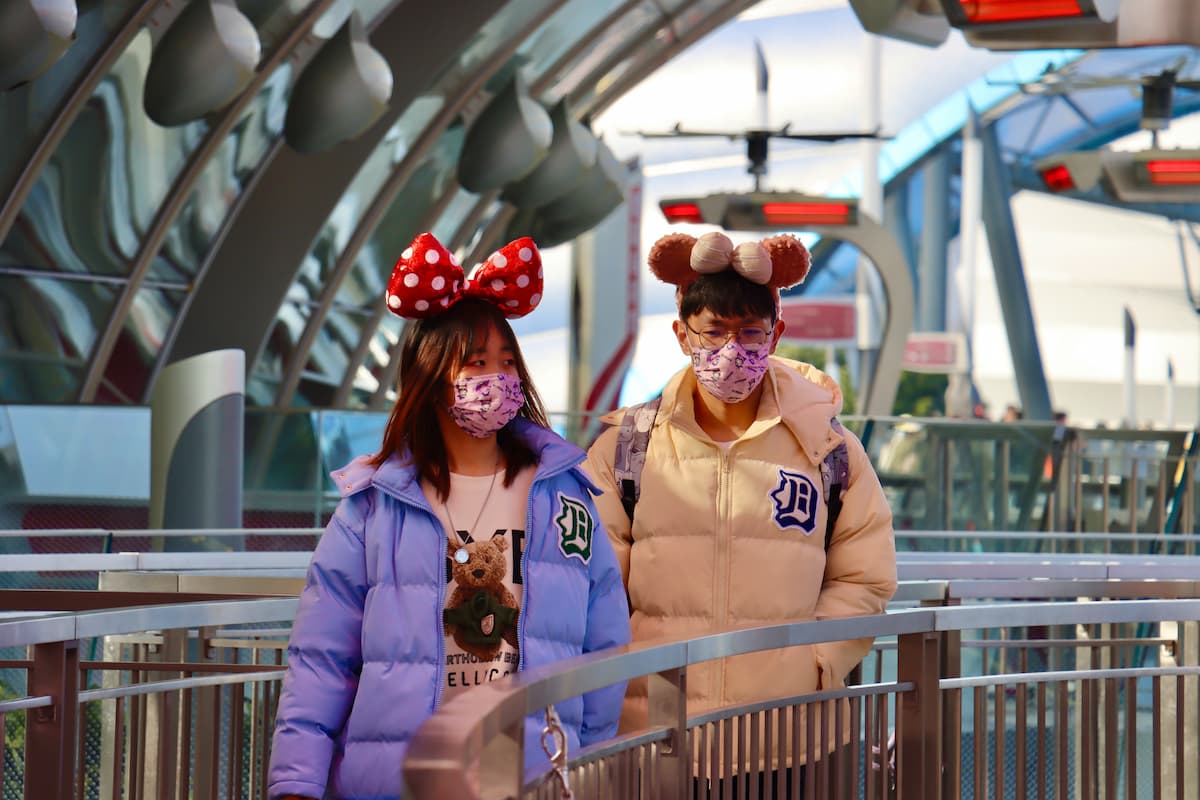 Two teenagers wearing Minnie Mouse ears and mask in Disneyland.